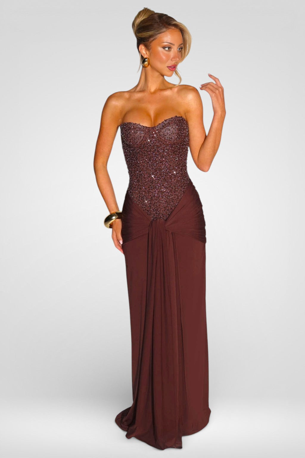 Woman wearing a strapless, sequined burgundy evening gown on a white background