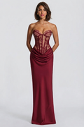 A woman modeling a strapless floor-length gown with a lace corset-style bodice and draped satin skirt in a deep burgundy red, photographed against a light gray studio background.