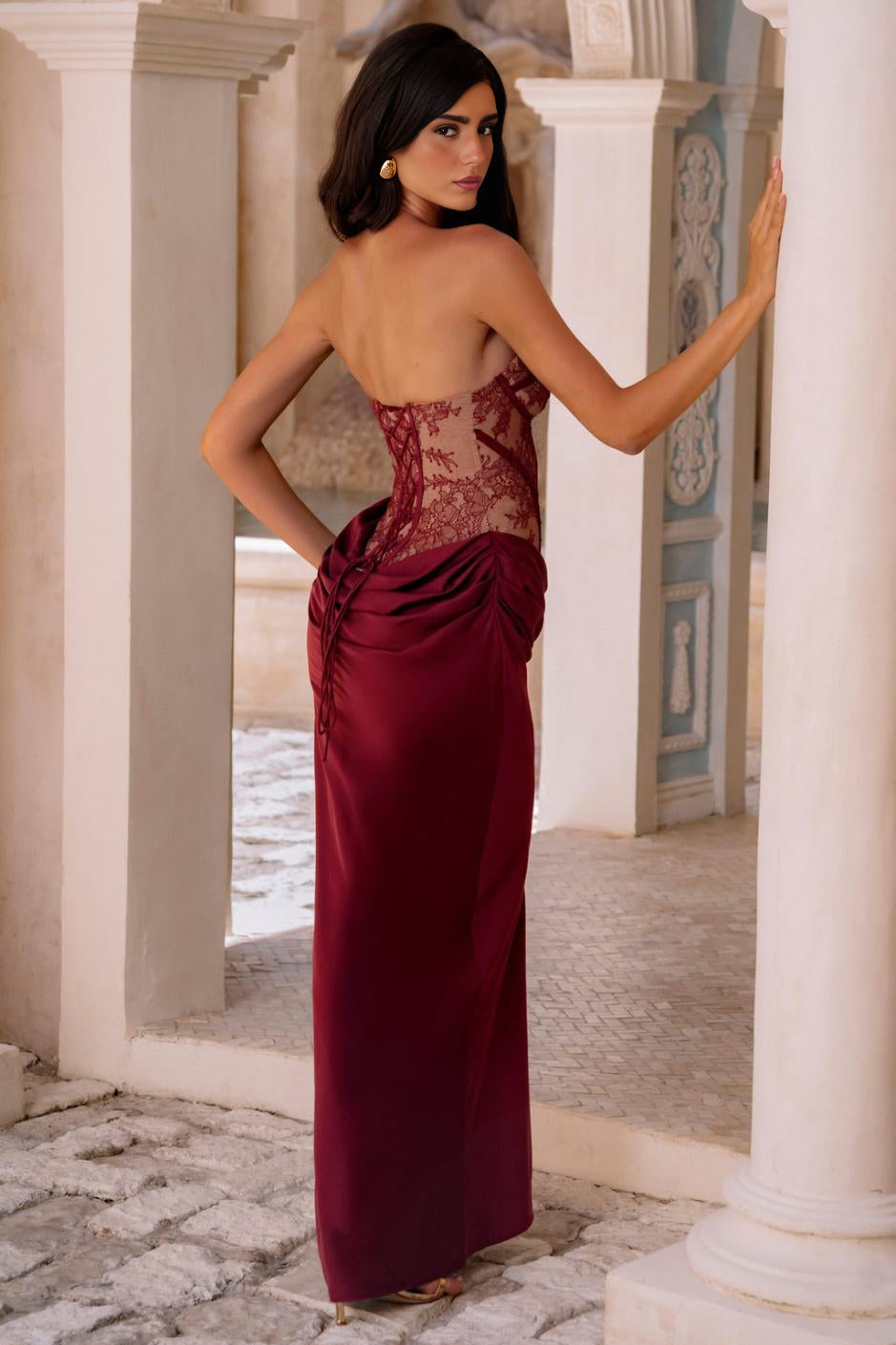 Woman in a burgundy evening gown standing in an architectural setting with columns.