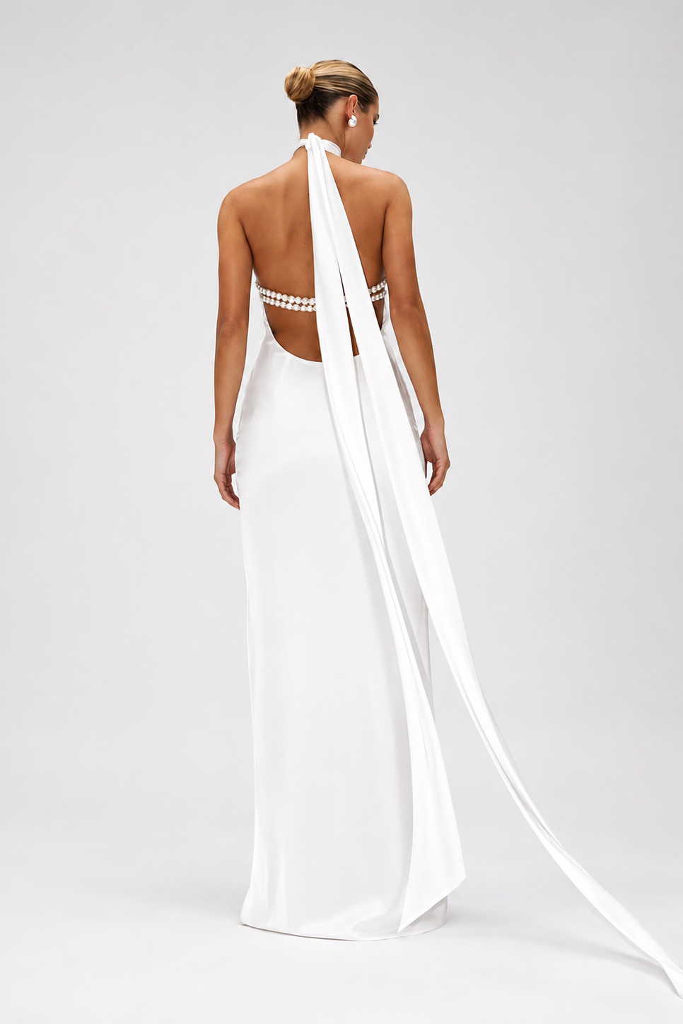 Woman wearing a white wedding dress with a long train on a plain background