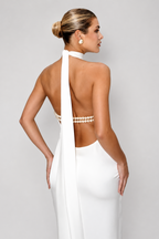 Woman wearing a white dress with a pearl embellished back on a plain background