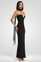 Woman wearing a black strapless gown with a slit on a white background