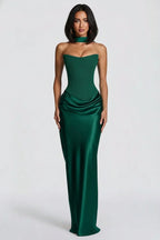 A woman modeling a strapless emerald green satin gown with a sweetheart neckline, structured corset-style bodice, ruched waist, and a matching choker, photographed against a light gray studio background.