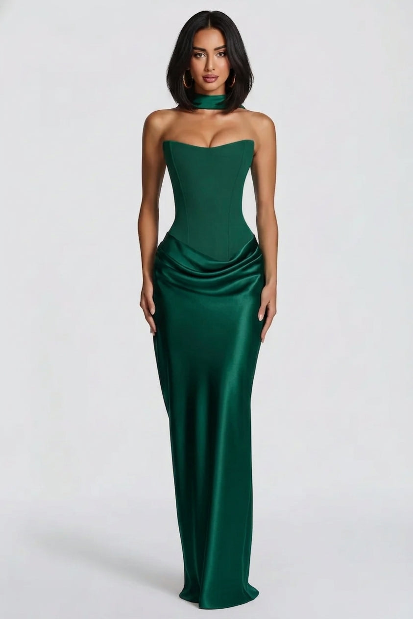 A woman modeling a strapless emerald green satin gown with a sweetheart neckline, structured corset-style bodice, ruched waist, and a matching choker, photographed against a light gray studio background.