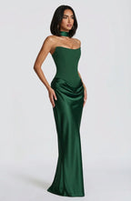 A woman modeling a strapless emerald green satin gown with a sweetheart neckline, high neck choker, and draped skirt details, set against a plain light gray studio background.