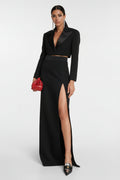 Black outfit with a high slit skirt and red handbag on a white background