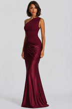 A woman modeling a floor-length, one-shoulder satin gown in deep burgundy against a light gray studio background.