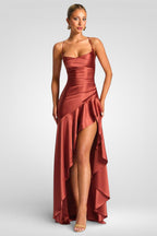 Woman wearing a rust-colored evening gown with a high slit on a light gray background