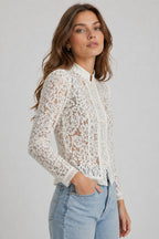 Woman wearing a white lace top and light blue jeans against a plain background