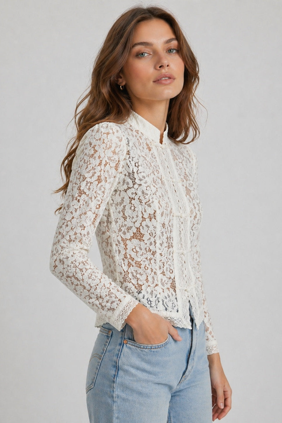 Woman wearing a white lace top and light blue jeans against a plain background