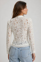 Woman wearing a white lace top and blue jeans on a plain background