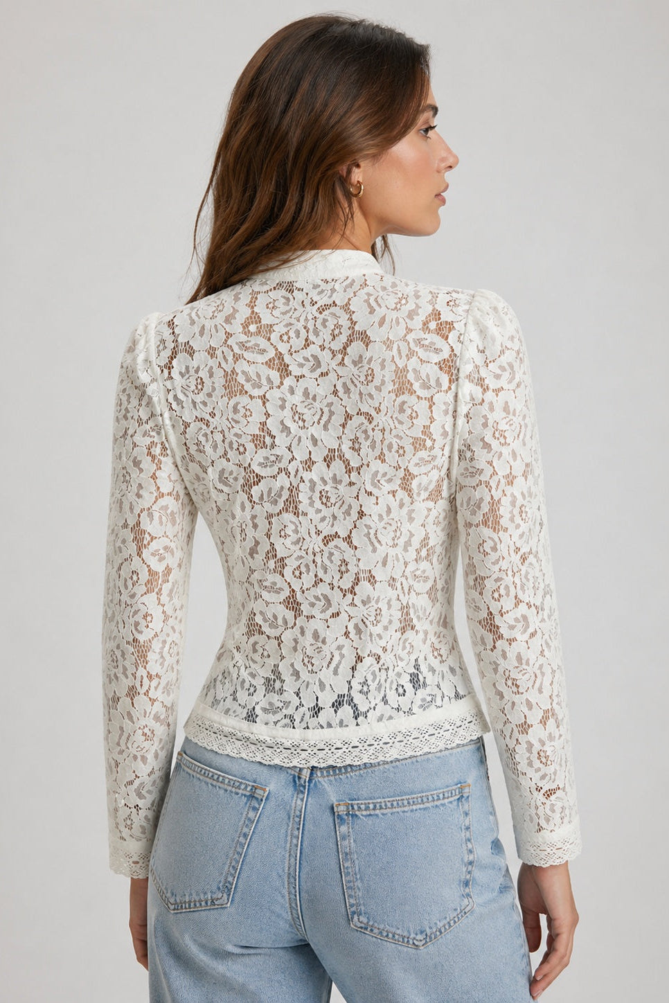 Woman wearing a white lace top and blue jeans on a plain background