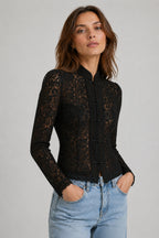 Woman wearing a black lace top and light blue jeans against a gray background