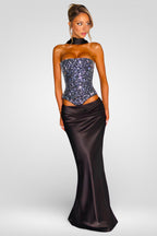 Woman wearing a strapless sequined top and long satin skirt on a white background