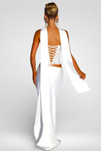 Woman wearing a white dress with a lace-up back on a plain background
