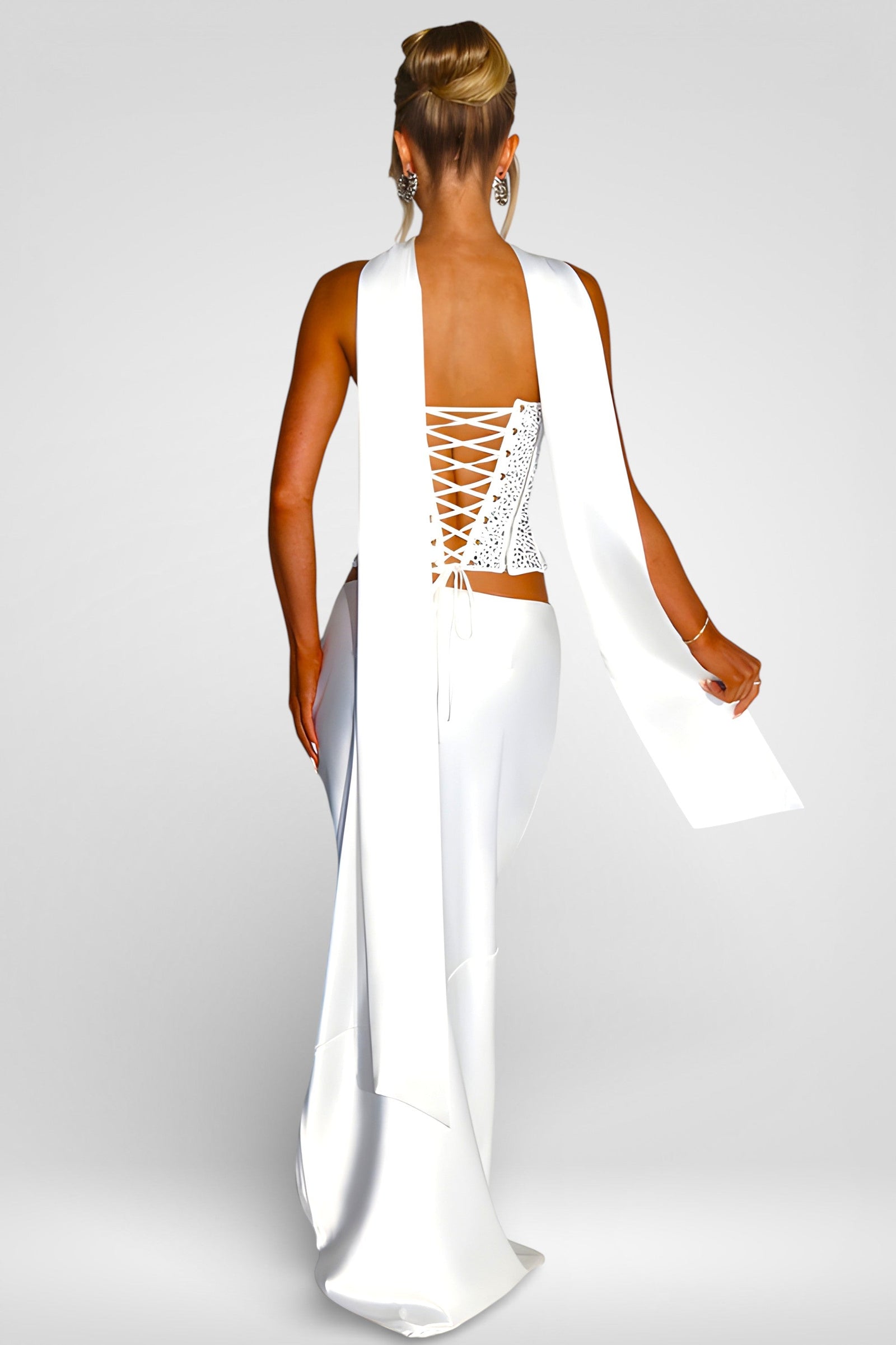 Woman wearing a white dress with a lace-up back on a plain background