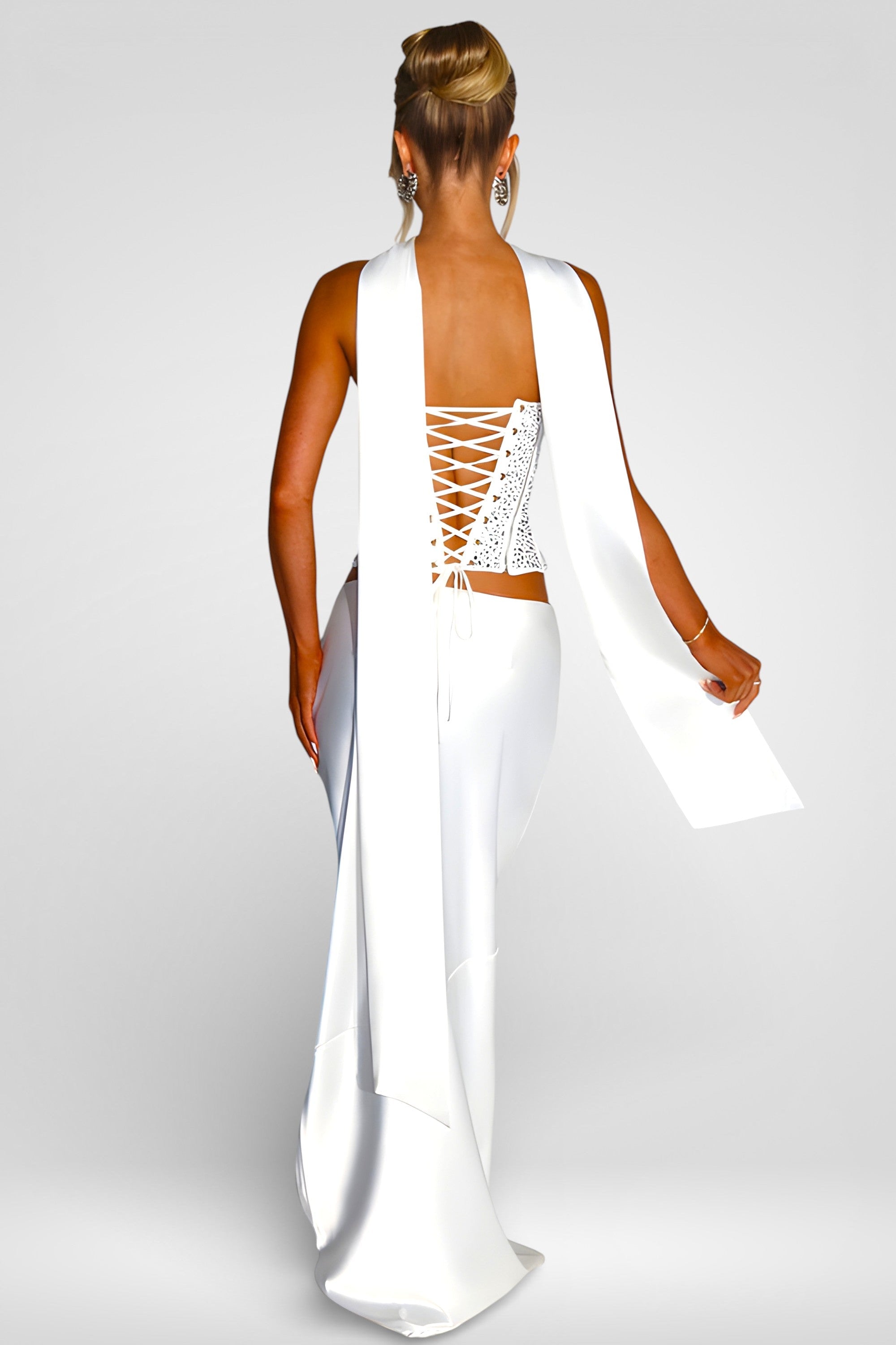 Woman wearing a white dress with a lace-up back on a plain background