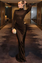Woman in a long, dark brown dress standing in a modern interior setting.
