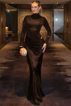 Woman in a brown evening gown standing in an elegant interior setting.