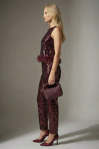 Woman wearing a burgundy sequin jumpsuit with matching shoes and handbag against a gray background