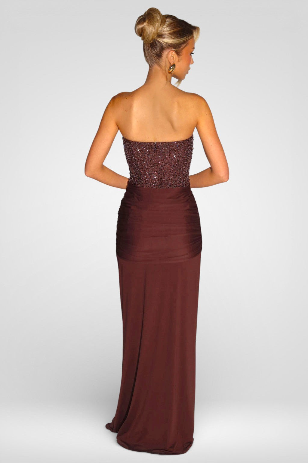 Woman wearing a strapless brown evening gown with sequined top on a white background