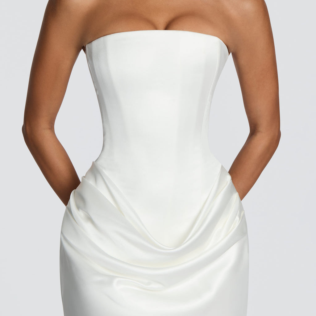 A strapless white satin mini dress with a structured corset-style bodice and draped skirt, shown on a model against a light gray studio background.