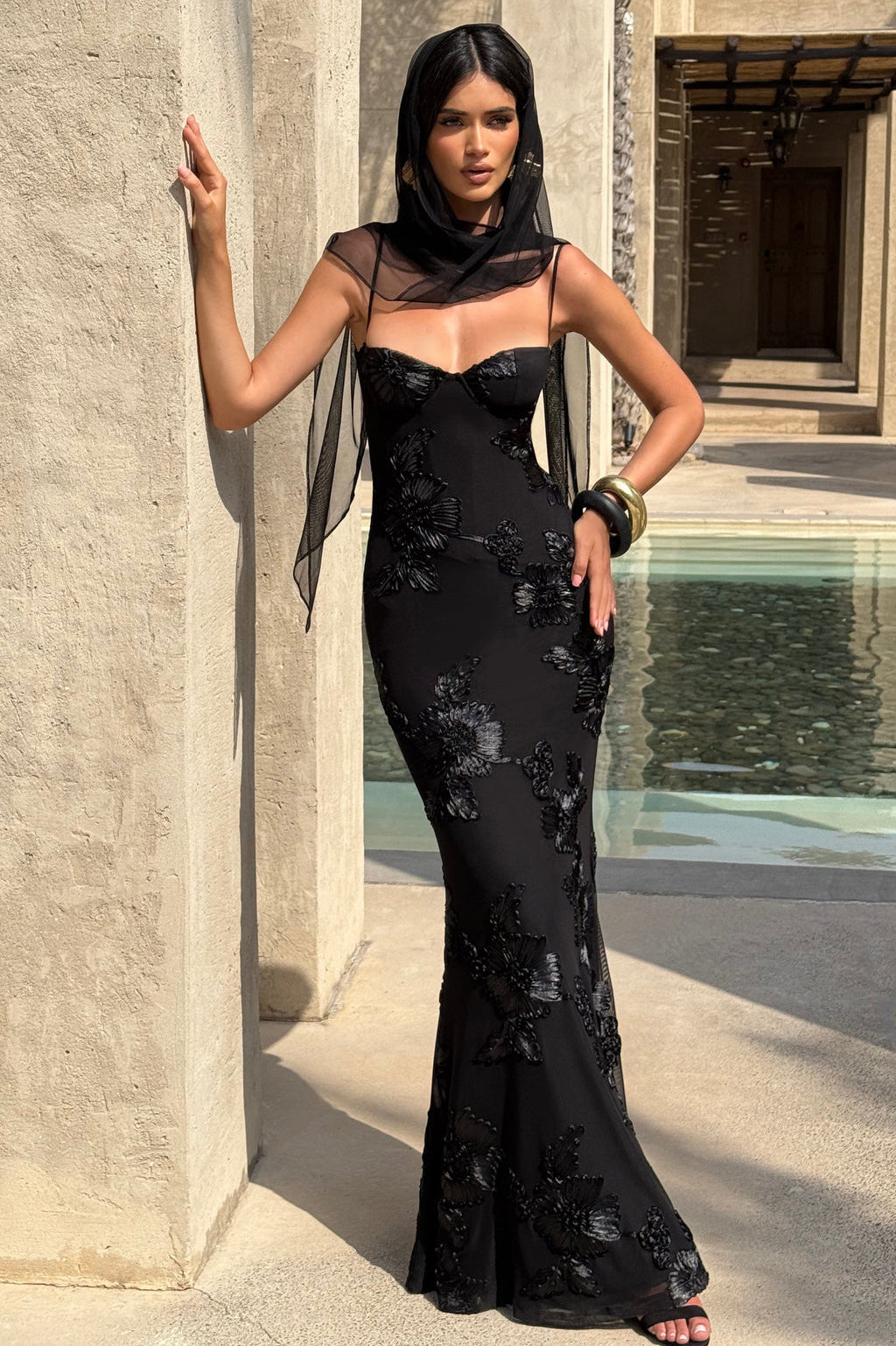 Woman in a black evening gown standing against a stone wall with water feature.