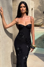 Woman in a black floral dress standing against a stone wall with a pool in the background